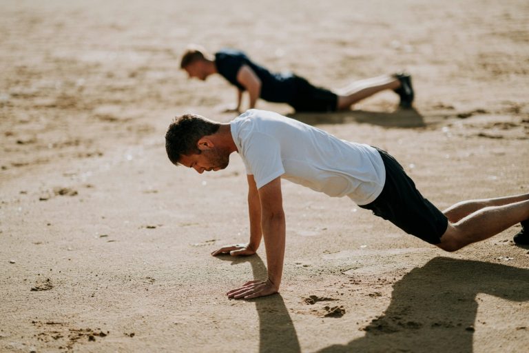 Two men doing push-ups on a sandy beach.