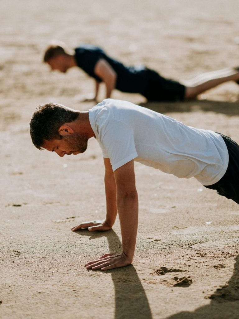 Two men doing push-ups on a sandy surface.