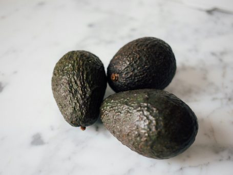 Three dark green avocados on a marble surface.