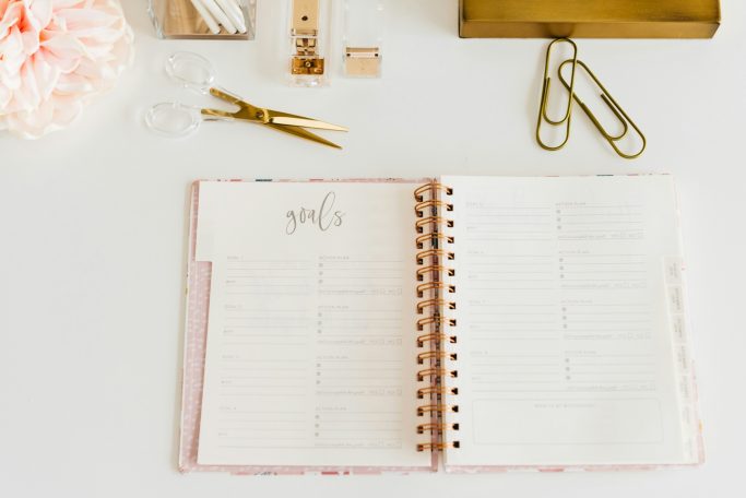 Open planner on a desk with stationery tools and clips nearby.