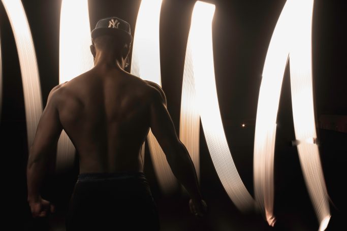 A muscular figure facing a backdrop of illuminated, flowing lines.