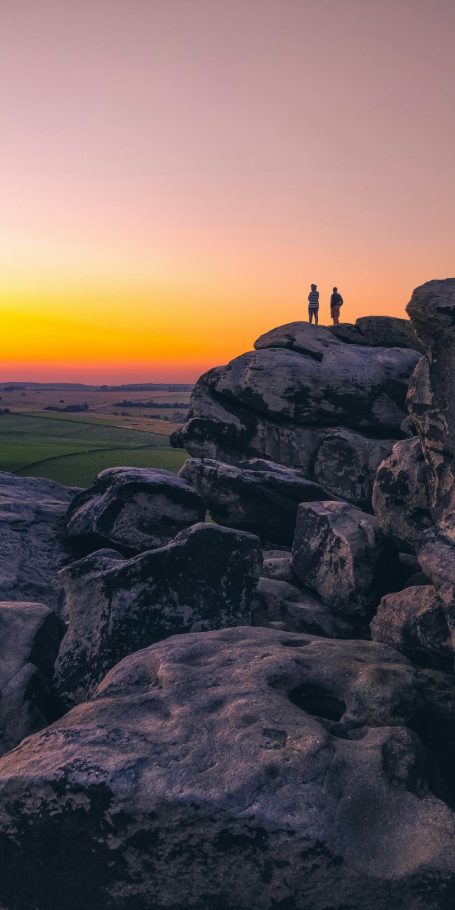 Silhouettes of three people on rocky outcrop at sunset with a vibrant sky.