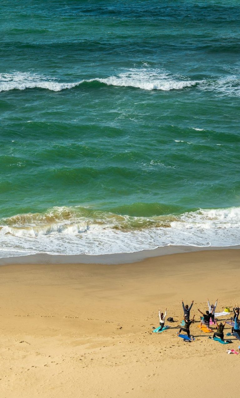 Group of people sitting on a sandy beach near the ocean, with waves in the background.