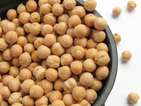 Raw chickpeas in a black bowl, with some scattered outside.