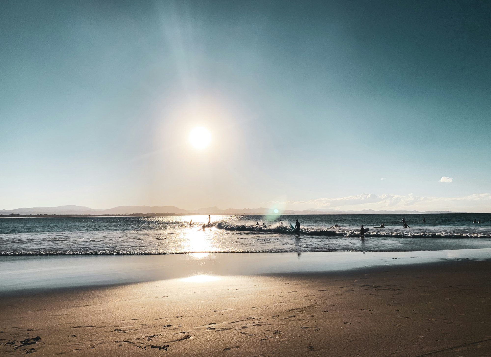 Sunset over a calm beach with silhouettes of people walking along the shore.