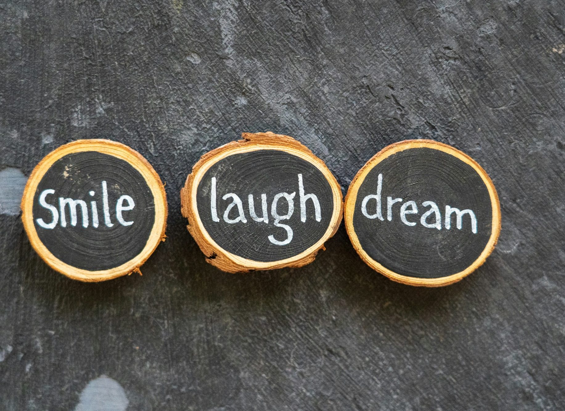 Words "Smile", "Laugh", and "Dream" written on wooden slices.