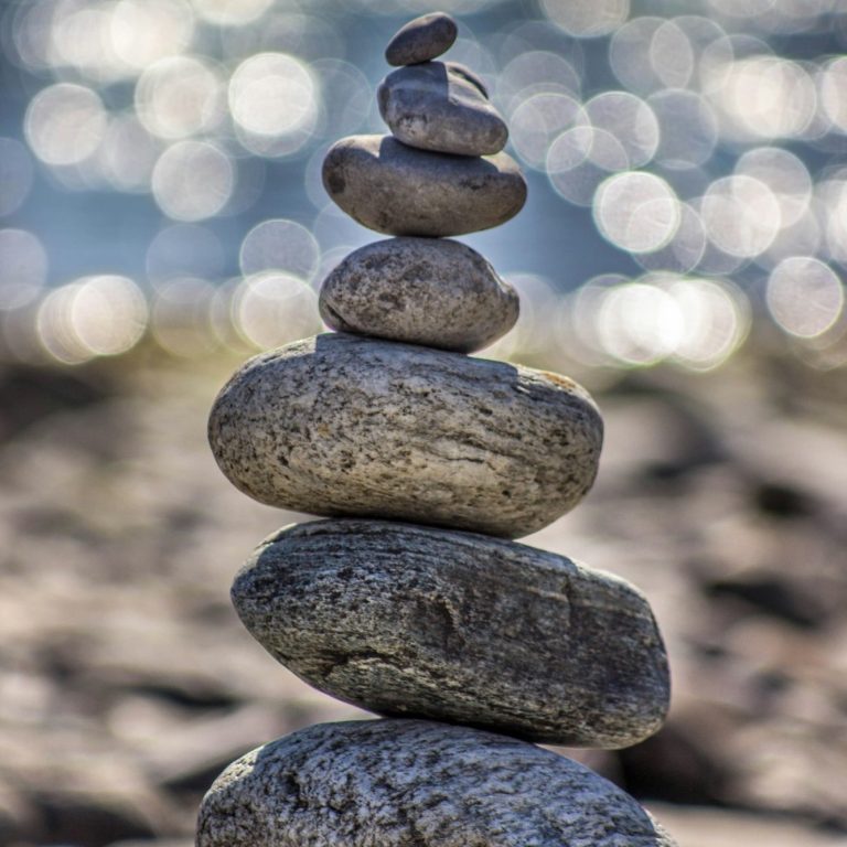 A stack of smooth stones balanced on a pebbly surface, with a sparkling water background.