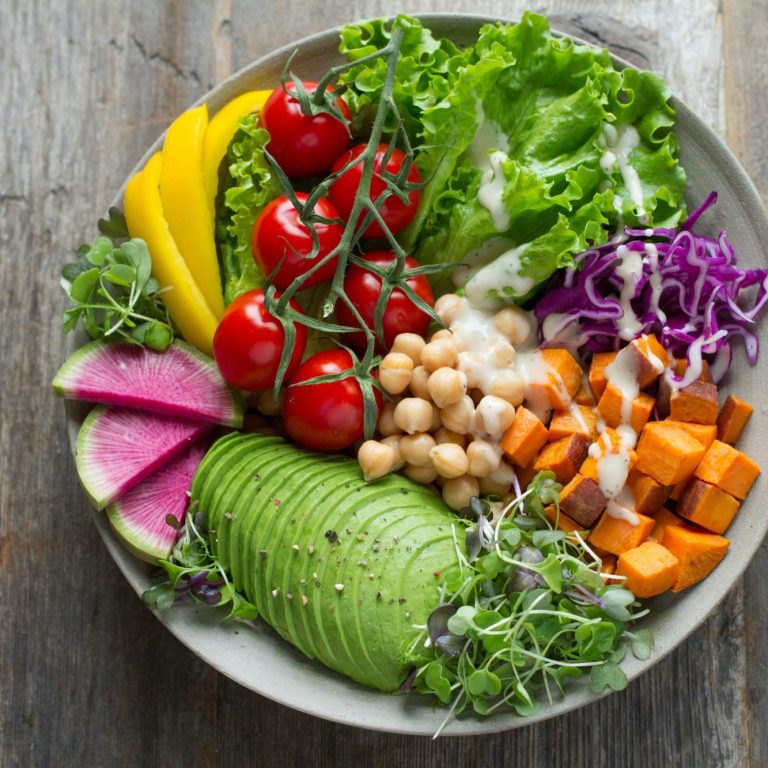 A vibrant salad with greens, tomatoes, avocado, sweet potato, and assorted vegetables.