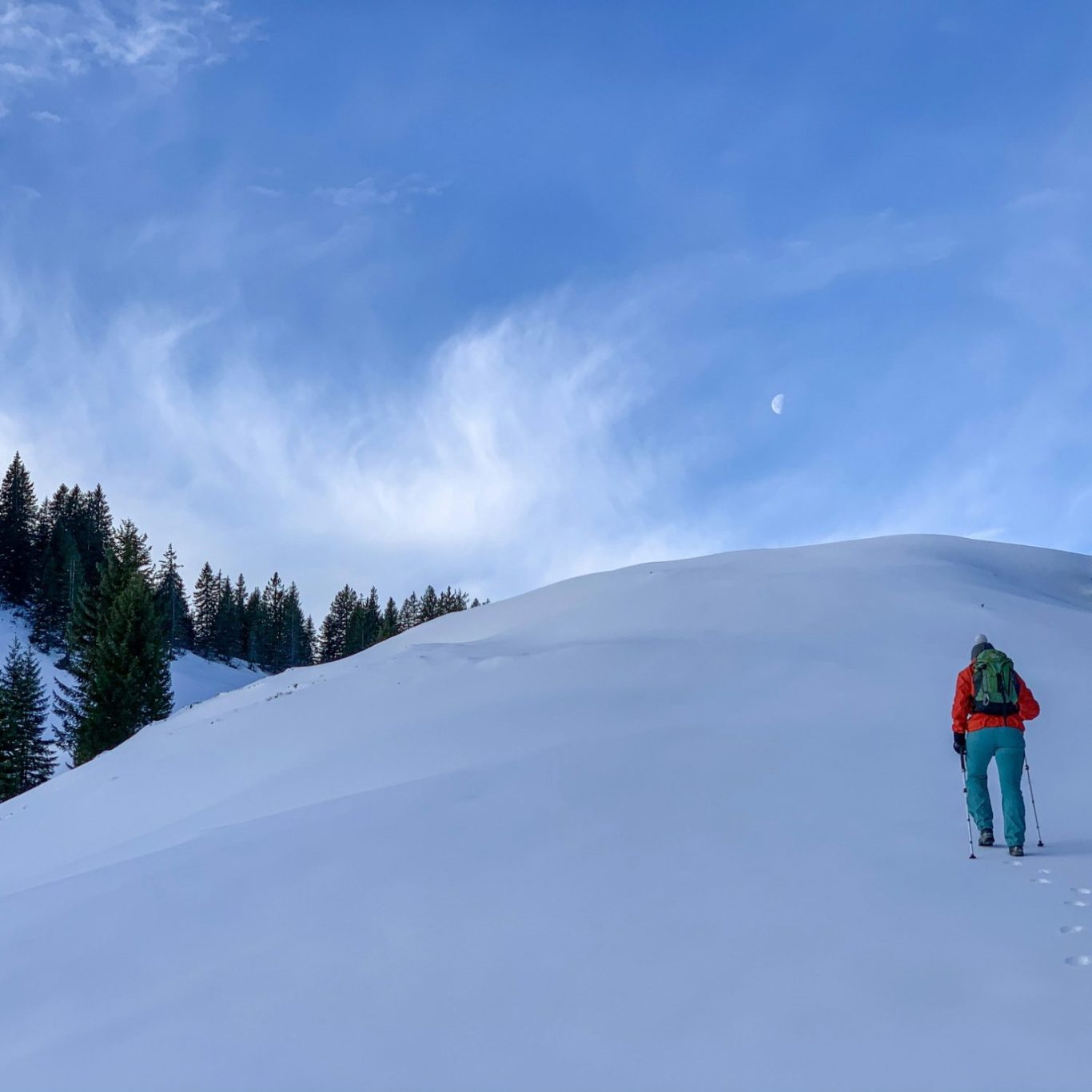 Person hiking up a snowy slope with a blue sky and wispy clouds above.