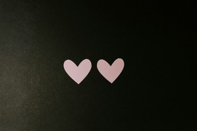 Two pink paper hearts on a dark background.