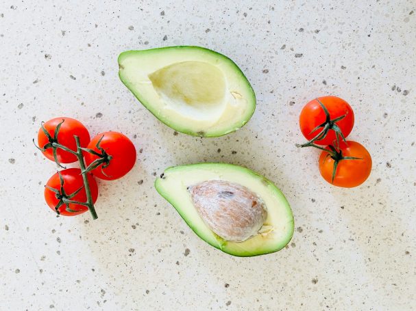 Halved avocado with pit, surrounded by cherry tomatoes on a light surface.