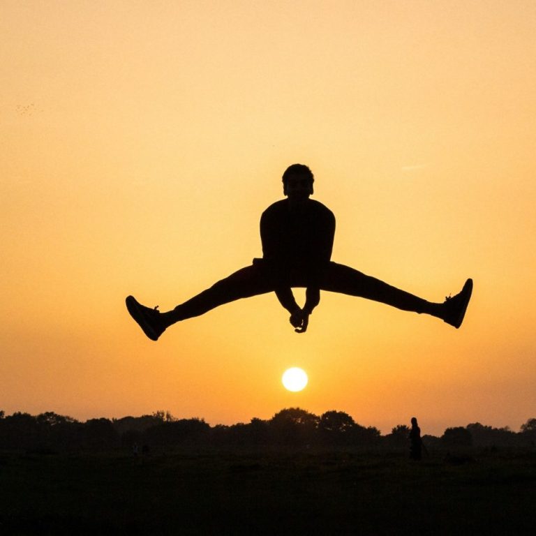 Silhouetted figure jumping against a vibrant sunset with a golden horizon.