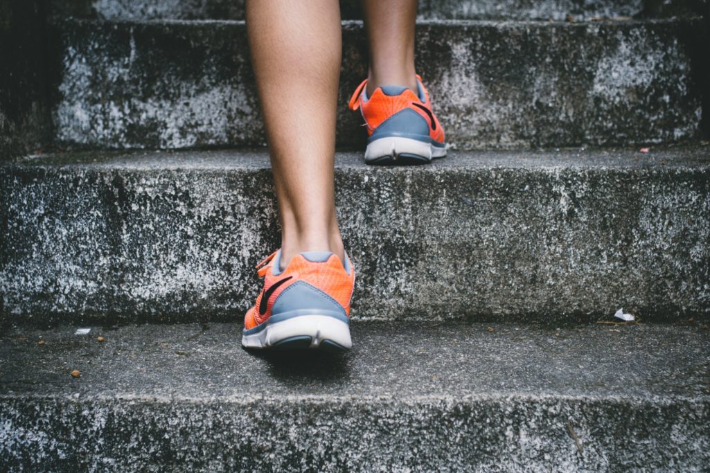 A person in grey and orange trainers walking up worn stone steps.