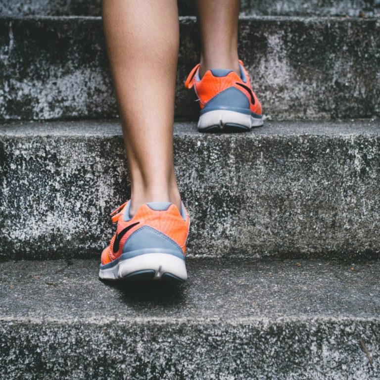 A person walking up concrete stairs in bright running shoes.